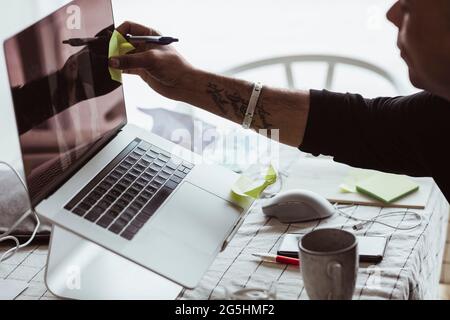 Cropped image of businessman sticking adhesive note on device screen during video conference at home Stock Photo