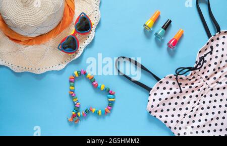 Summer composition. Sunglasses, hat, polka dot swimsuit, nail polish and a heart made of beads on a blue background with copy space. Vacation concept Stock Photo