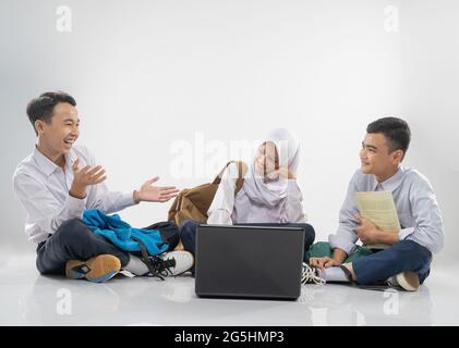 three teenagers in junior high school uniforms sitting on the floor studying together with joking when using a laptop Stock Photo