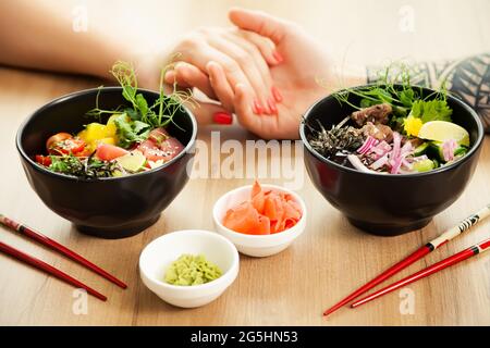 Loving couple man and woman eating salad poke chopsticks. Place the tuna salad in a bowl. People in the restaurant eat salad with chopsticks. Asian Stock Photo