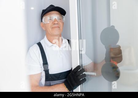Happy joinery worker man installs plastic upvc windows with three glazed white. Stock Photo