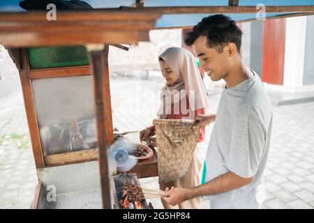 two seller preparing food on their food stall selling traditional chicken satay Stock Photo
