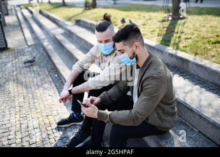 Men friends outdoors on street in town using smartphone, coronavirus and new normal concept. Stock Photo