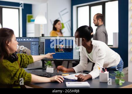 Diverse women game software developers creating game interface sitting in startup creative agency company pointing at pc displays. Workers developing online video games with modern technology Stock Photo