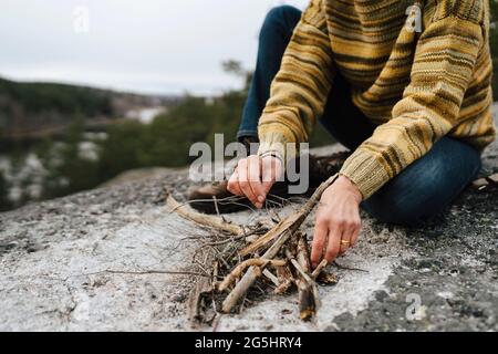Low section of woman with sticks preparing campfire at mountain Stock Photo