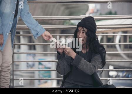 Homeless beggar man begging for money, food and help on street. Poverty despair poor man hungry and loneliness need help from man kind. woman give mon Stock Photo