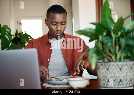 Young African man using a laptop while eating breakfast Stock Photo