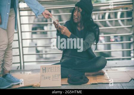 Homeless beggar man begging for money, food and help on street. Poverty despair poor man hungry and loneliness need help from man kind. woman give mon Stock Photo