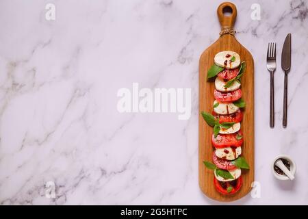 Italian caprese salad with sliced tomatoes, mozzarella, basil, olive oil on a wooden serving board. Stock Photo