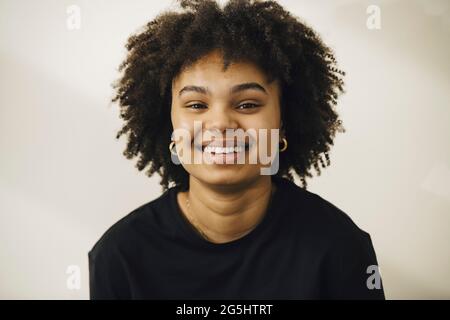 Smiling young woman with curly hair against beige background Stock Photo