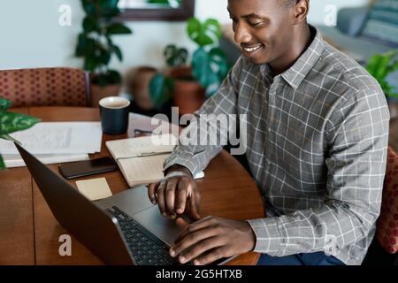 Smiling young African businessman working from home using a laptop Stock Photo