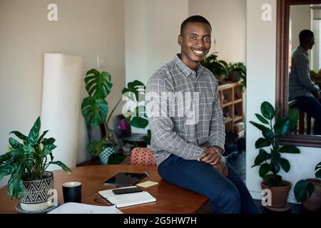 Smiling African businessman sitting on a table while working from home Stock Photo