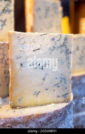 Stacks of whole and cut Stilton cheeses for sale at a market. This is a popular English blue cheese that has had Penicillium roqueforti added to creat Stock Photo