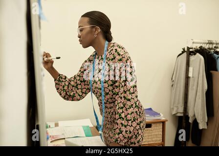 Young African female clothing designer writing notes on a whiteboard Stock Photo