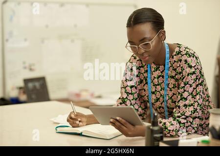 African female clothes designer working on a tablet in her studio Stock Photo