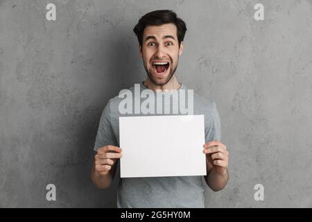 Handsome young man with a white blank board isolated over gray Stock Photo