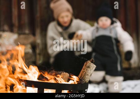 Burning wood in fire pit against woman and daughter during winter Stock Photo