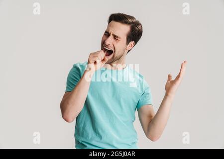 Cheerful young casual man singing with pretend microphone isolated over gray background Stock Photo