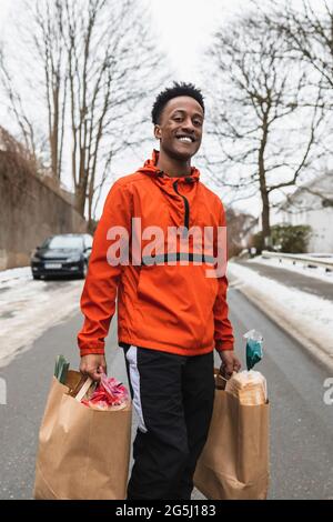 Portrait of smiling essential service male carrying paper bags while walking on road Stock Photo