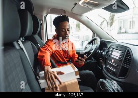 Young male driver using smart phone while sitting in delivery van Stock Photo