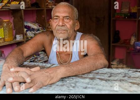 Beautiful photo of thoughtful Indian male, senior citizen by age, posing at camera while sitting in his shop and waiting for customers. Stock Photo