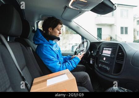 Female driver using smart phone while sitting in delivery van Stock Photo