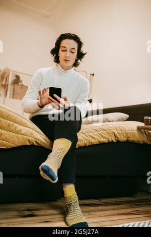 Man using smart phone while sitting bedroom at home Stock Photo