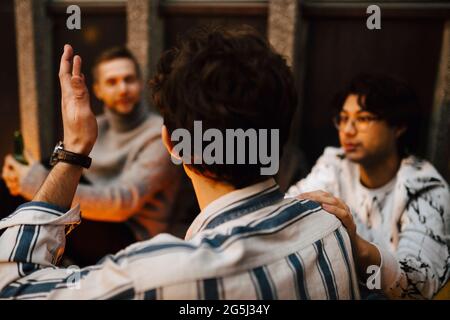 Rear view of man gesturing while talking with friends at balcony Stock Photo