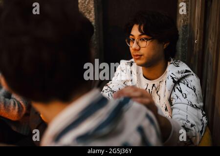 Young man sitting with hand on male friend's shoulder at balcony Stock Photo