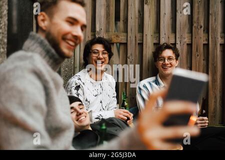 Smiling male friends taking selfie through smart phone in balcony Stock Photo