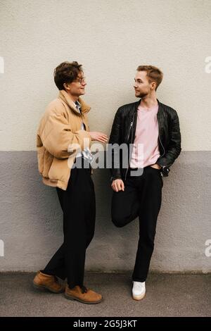 Male friends talking with each other while leaning on beige wall Stock Photo