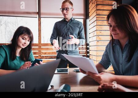 Young businessman speaks in front of an audience in a modern office about the development of start-up - Leader talks with colleagues at a meeting - Mi Stock Photo