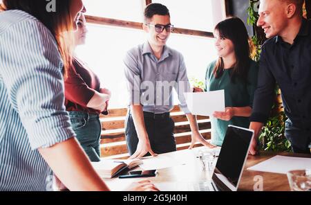 A group of young people are discussing a new business project in the office - Gathering of young creative people - Colleagues and employees working to Stock Photo