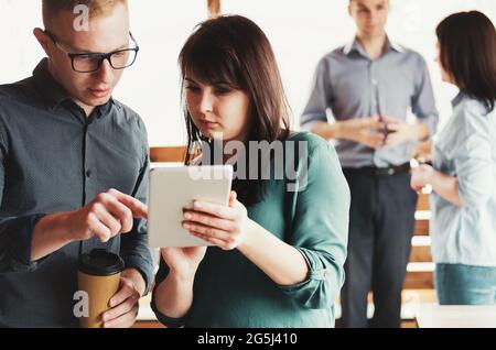 A man and a woman are discussing a project and looking into a tablet - Two young businessmen are talking in an office at a joint meeting - Young emplo Stock Photo