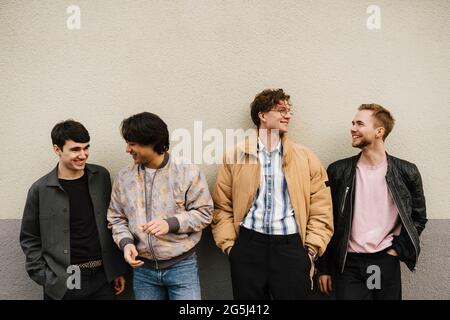 Happy multi-ethnic male friends talking while standing against wall Stock Photo