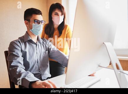 Two colleagues in the office are working on a new project with masks on their faces - Employees in the office wearing masks as protection against covi Stock Photo