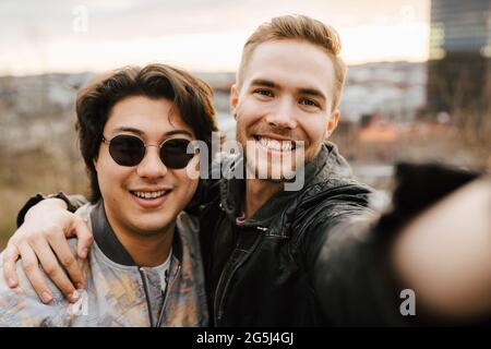 Young male friends smiling while taking selfie Stock Photo