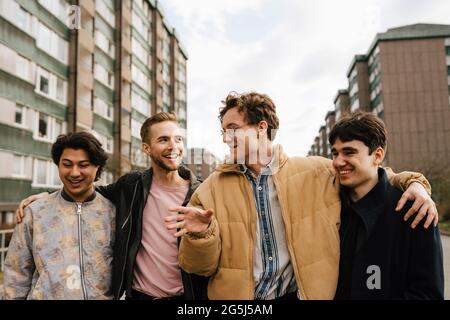 Smiling male friends talking while walking with arms around in city Stock Photo