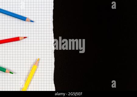Colored pencils on white squared torn sheet of paper over black school chalkboard. Back to school, education, learning concept. Top view, copy space Stock Photo