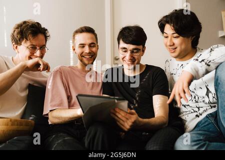 Smiling man using digital tablet while sharing with male friends in living room Stock Photo
