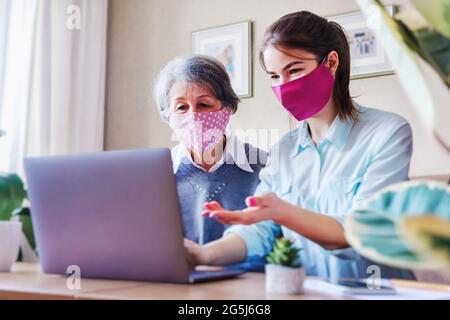 A positive adult daughter, together with an elderly gray-haired mother, sits on the couch and searches for useful information and content on the Inter Stock Photo