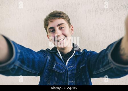 A teenager takes a selfie - a young man takes a picture of himself on a smartphone - a happy teenager takes a picture of himself on his phone made a h Stock Photo