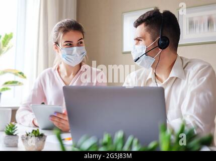 A man and a woman wearing masks on their faces work in a call center for customer service - Sales agents in the office or working remotely from home d Stock Photo