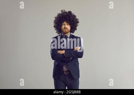 Serious business man in stylish curly hair wig standing with arms crossed Stock Photo