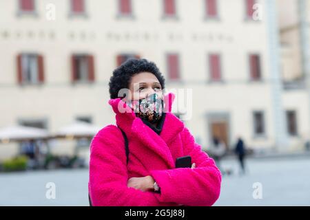 Italy, Tuscany, Pistoia, Woman in face mask and pink coat walking through city Stock Photo