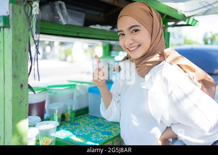 a pretty girl in a veil selling fruit ice smiles happily with a thumbs up Stock Photo