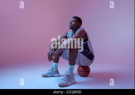 Basketball player sitting on ball in studio Stock Photo