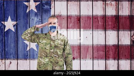 Composition of saluting male soldier wearing face mask, against american flag painted on wood boards Stock Photo