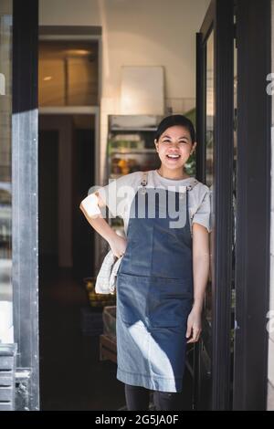 Portrait of smiling female owner with hand on hip standing at entrance of store Stock Photo