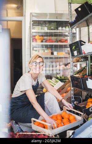 Portrait of smiling female owner arranging fruits in rack at store Stock Photo